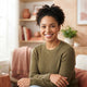 A smiling, diverse woman posing for a professional headshot in a bright, modern room with warm-toned decor.