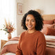 A friendly, diverse woman smiling confidently in a modern, well-lit room decorated with warm terracotta and rose accents.