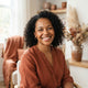 A smiling, diverse woman in a bright, modern room with warm-toned decor, representing a happy and satisfied customer.