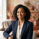A smiling, diverse woman posing for a professional headshot in a modern, warmly decorated interior space with soft terracotta